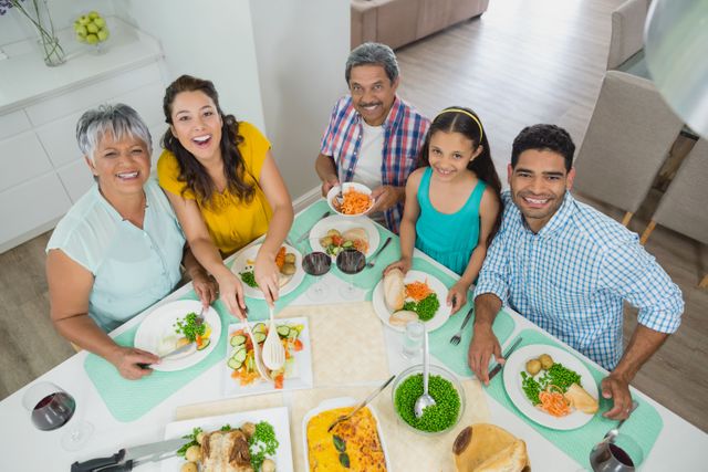 Multi-generation family gathered around dining table, enjoying meal together. Grandparents, parents, and children smiling and bonding over food. Ideal for use in advertisements, family-oriented content, lifestyle blogs, and articles about family values and togetherness.