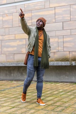 African american man pointing upward while walking on urban plaza wearing beanie and scarf
