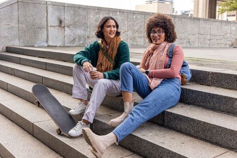 Friends chatting on city steps with skateboard and casual fall fashion