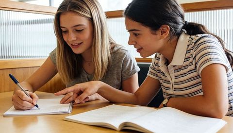 Teen girls studying together in library booth writing notes and collaborating on homework