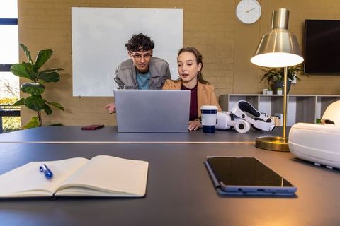 Colleagues collaborating on laptop with vr headset and notebook in modern coworking space