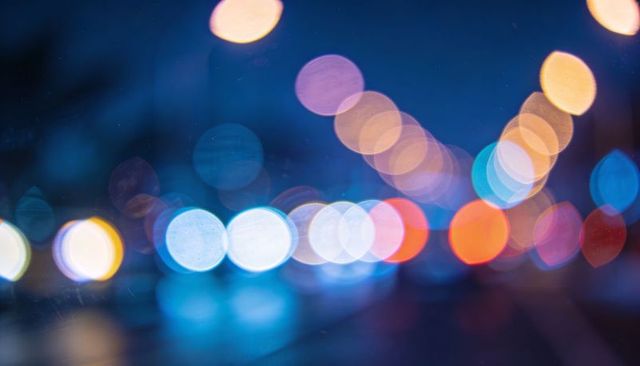 Glowing bokeh lights reflecting on wet urban pavement at night, multicolor traffic blur