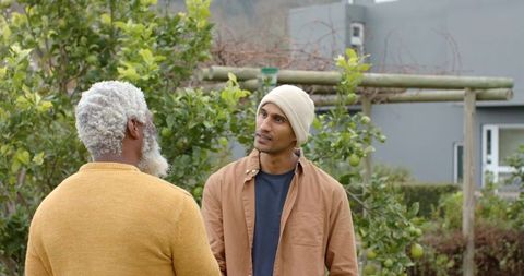 Diverse men talking in backyard fruit garden, neighborly conversation, casual clothing