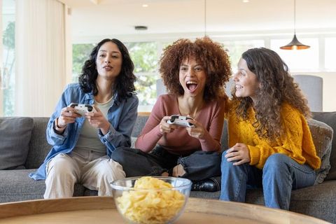 Diverse friends gaming night on couch laughing with controllers and chips