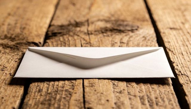 Resting white envelope lying on rustic wood planks under warm golden light