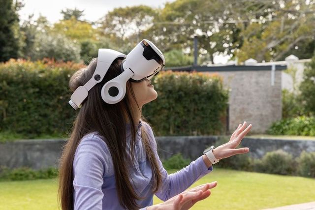 Young asian woman trying virtual reality in backyard wearing white vr headset and smartwatch