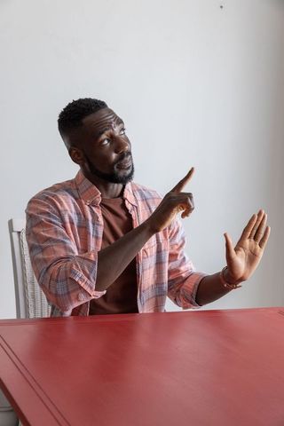 Man Wearing Pink Plaid Shirt Gesturing at Red Table
