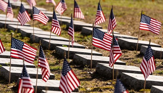 American flags fluttering over veteran grave markers in sunlit cemetery rows memorial day