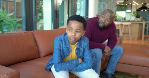 African american father and son sitting on couch showing family tension and distance