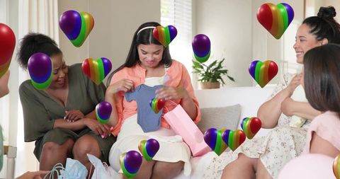 Expectant mother unwrapping baby onesie at cozy baby shower surrounded by smiling friends