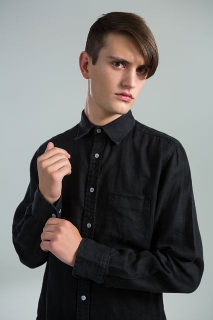 Androgynous man adjusting his hand cuffs against grey background