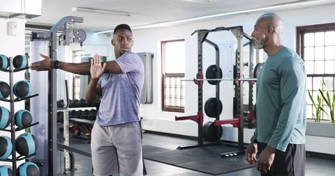 Trainer guiding athlete stretching shoulders in gym