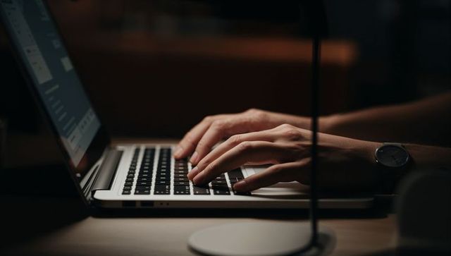 Hands typing on laptop keyboard at night showing focused work, productivity, wristwatch