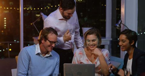 Team Collaborating on Laptops at Night in Office with Skyline View