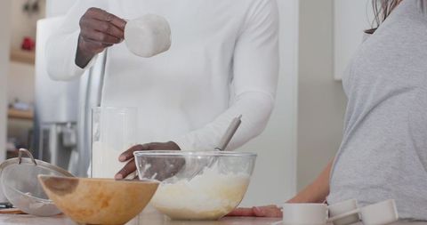 African american man pouring milk while partner preparing batter on kitchen countertop