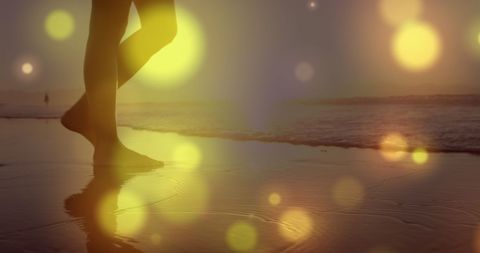 barefoot woman strolling along a serene beach during sunset, with enchanting yellow bokeh lights creating a dreamy atmosphere. ideal for use in themes related to relaxation, romance, and contemplative solitude.