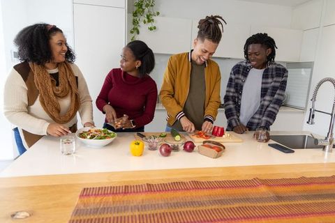 Multiracial friends chopping vegetables and tossing salad on modern kitchen island
