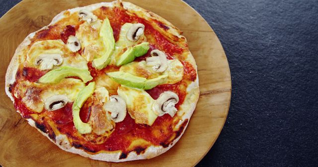 Homemade Neapolitan pizza topped with tomato sauce, cheese, avocado slices, and mushrooms on a wooden table. Ideal for culinary blogs, recipe books, and food advertisements showcasing unique topping combinations.