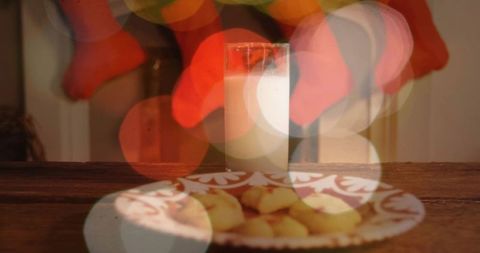 Milk and cookies on rustic table with christmas stockings and warm bokeh lights