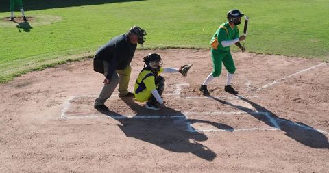 Youth baseball batter catcher umpire at home plate on sunlit community diamond