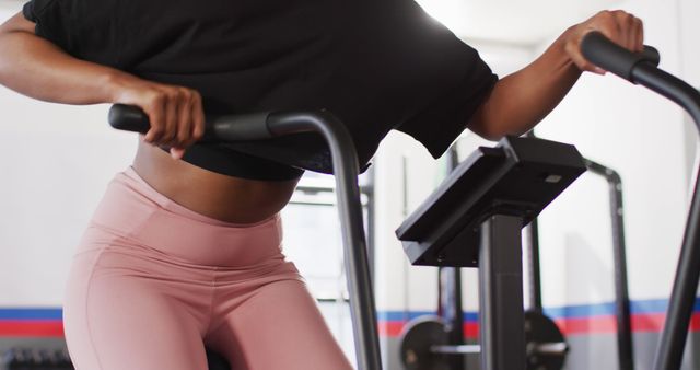 This closeup shot features a woman working out on an elliptical trainer in a modern gym. She is wearing pink leggings and appears to be determined. Ideal for use in fitness and health promotions, workout guides, and gym advertisements.