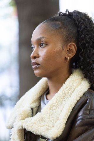 African woman gazing left, wearing shearling leather jacket and gold hoop earrings, contemplative