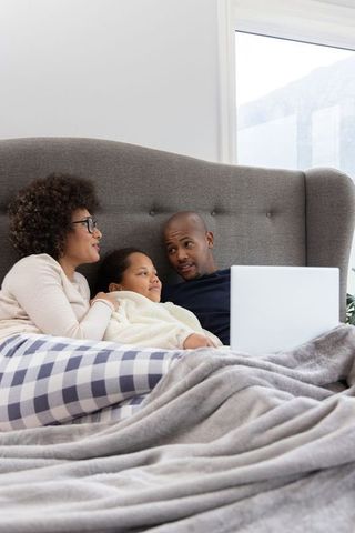 African american family cuddling in bed watching laptop, cozy morning at home together