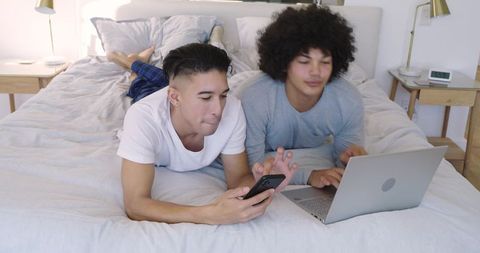 Roommates Relaxing with Technology on a Cozy Bed