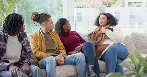 Young diverse friends sharing conversation on sunlit living room sofa during cozy hangout