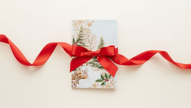 Holiday card featuring winter trees and deer wrapped with satin red bow on cream tabletop