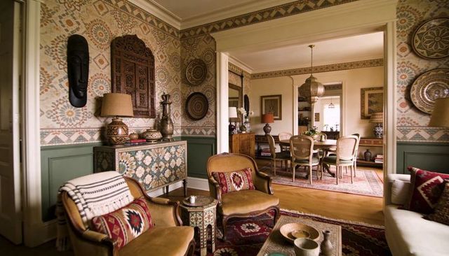 Carved wooden armchairs in ornate living space opening to dining area with patterned wallpaper