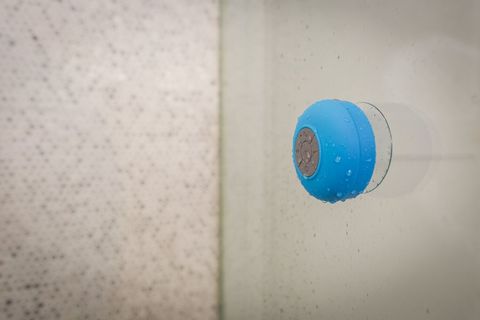 Blue waterproof bluetooth shower speaker sticking to glass with water droplets