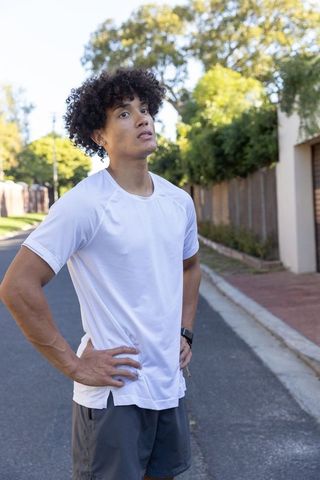 African american male runner resting on suburban sidewalk