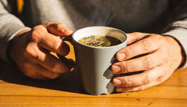 Sunlit hands cradling steaming herbal tea mug on wooden table cozy morning ritual