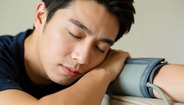 Relaxing asian man reclining with blood pressure cuff on arm for health monitoring