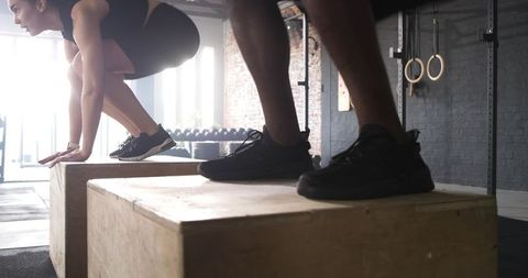 Diverse partners executing plyometric box jumps at gym