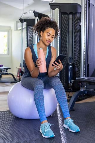 Woman Exercising in Gym Relaxing on Stability Ball Checking Smartphone