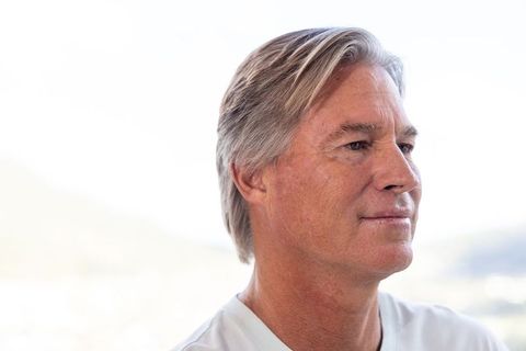 Mature man gazing at coastline wearing light crew-neck shirt, contemplative headshot