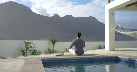 Indian man meditating on rooftop pool deck with mountain view, wellness and mindfulness