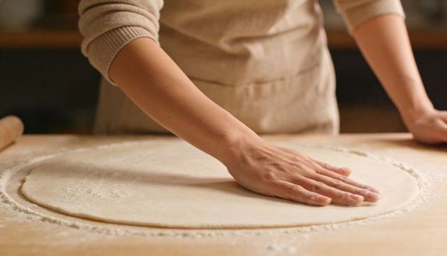 Home Baker Smoothing Rolled Dough on Wooden Countertop with Flour Ring and Rolling Pin