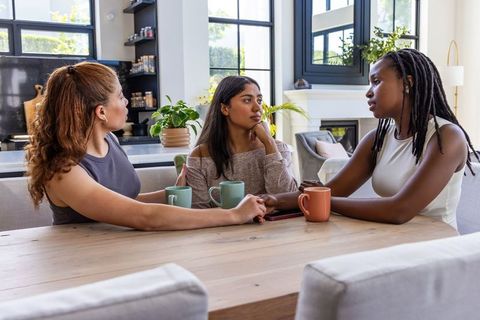 Diverse women having heartfelt conversation over coffee at bright modern kitchen table