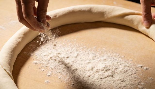 Sprinkling flour while shaping artisan dough ring on wooden countertop for bread