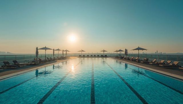 Rooftop infinity pool reflecting sunrise over city skyline with lounge chairs and parasols