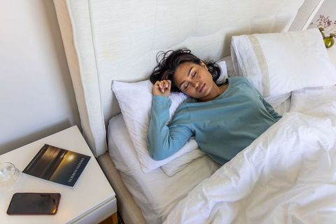 Indian woman sleeping peacefully in minimalist bedroom with white bedding and teal loungewear