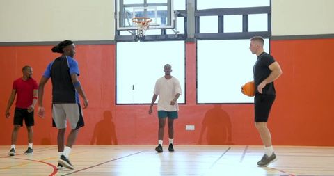 Playing pickup basketball indoors with group of athletic players on bright gym court