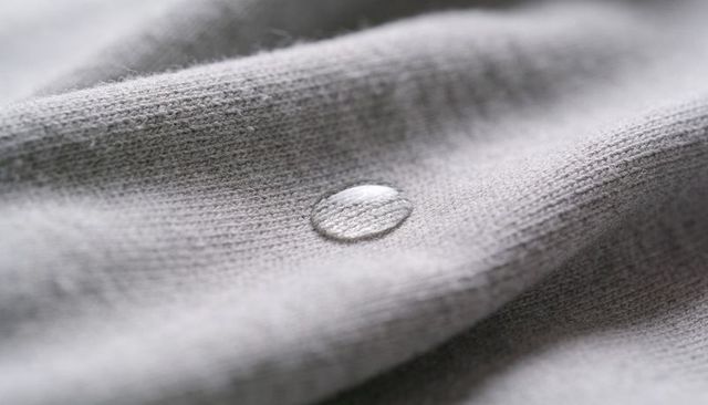 Water droplet beading on light gray knit fabric macro texture with ribbed detail
