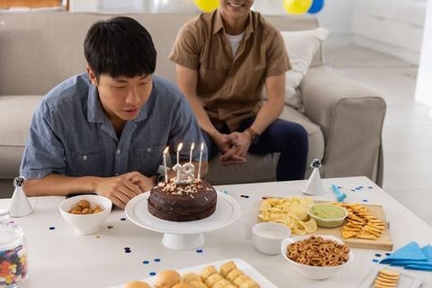 Asian young man blowing out 18th birthday candles while family celebrating at home