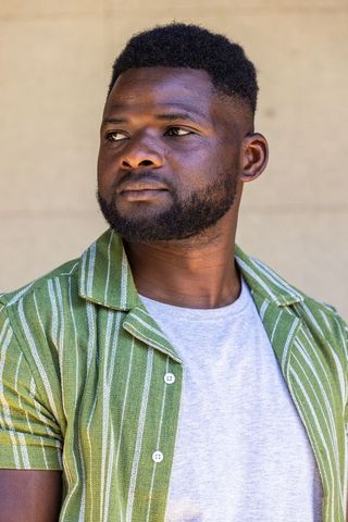 Confident man looking left wearing green striped shirt and gray tee outdoor headshot