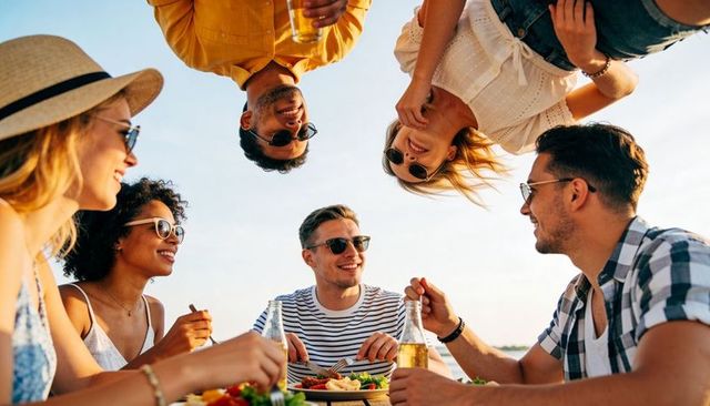 Friends chatting and sharing salad and beer at lakeside picnic during golden hour