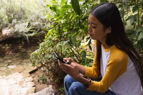 Young woman in garden using smartphone in natural surroundings